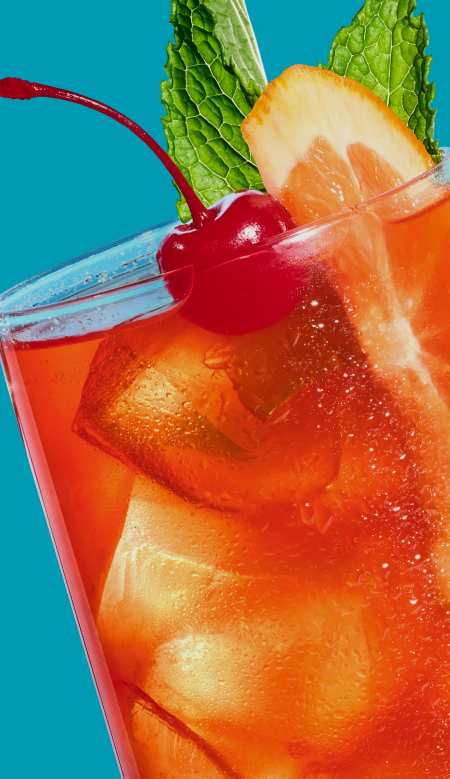 Chilled orange mocktail with ice, cherry, mint and orange slices on a bright blue background